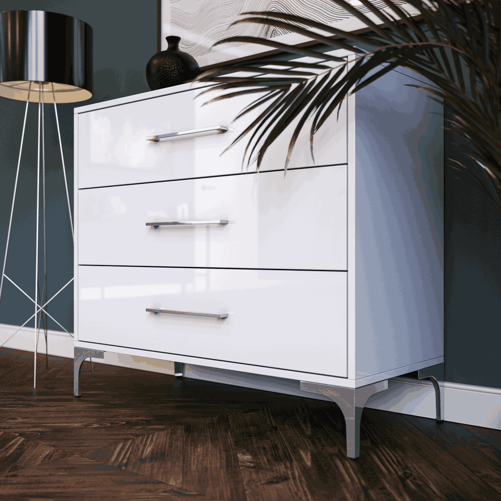 White dresser with silver legs and drawers against a dark wall with a plant and lamp.