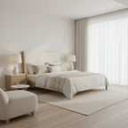 Modern bedroom with a bed, side table, and armchair in neutral tones.