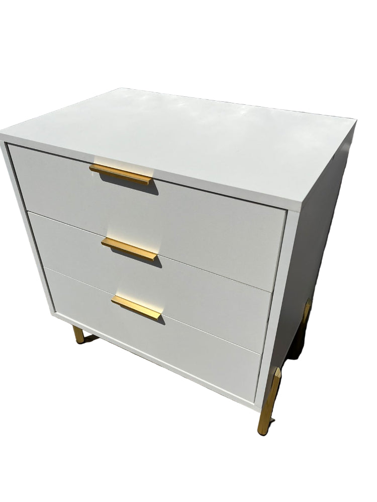 White dresser with gold handles against a textured wall.