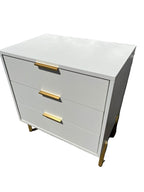 White dresser with gold handles against a textured wall.