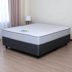 Mattress on a bed frame in a room with curtains and a lamp.